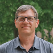 Photo of Brian Dingmann wearing a grey shirt and glasses